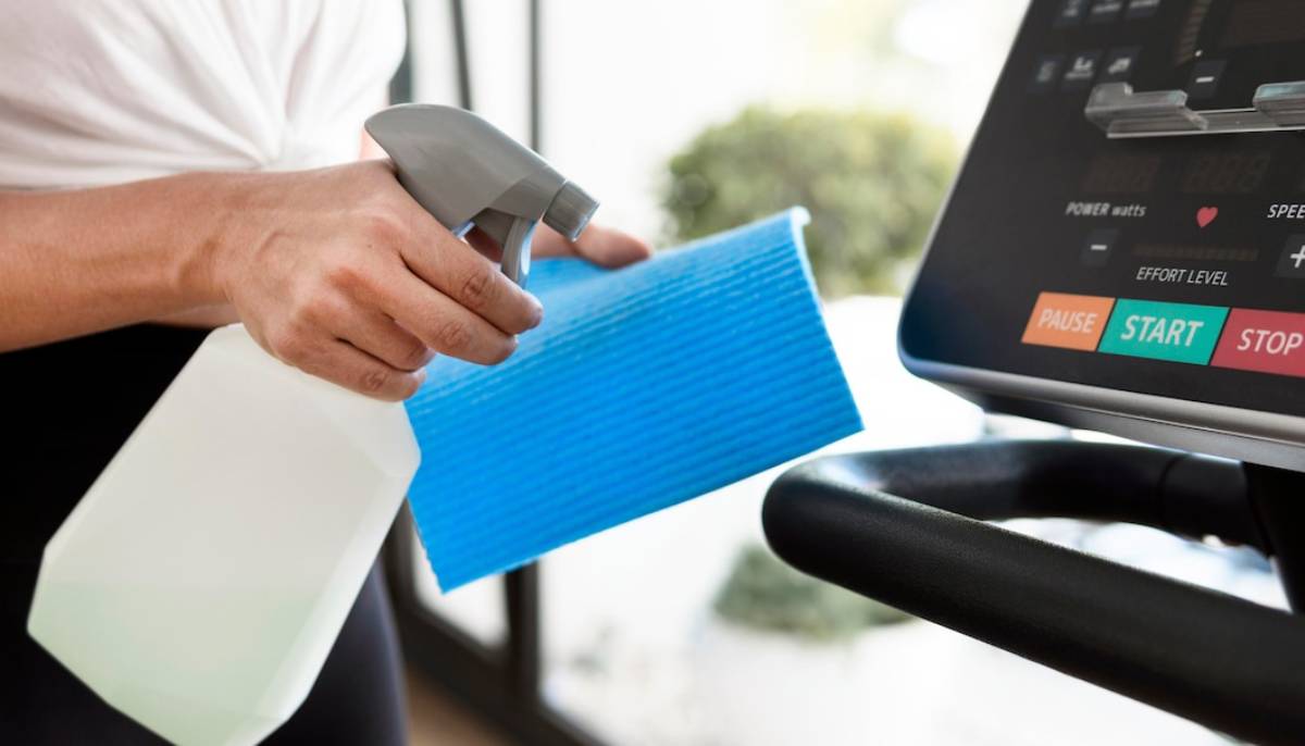 a person is holding spray and a cloth near a trademil to clean it