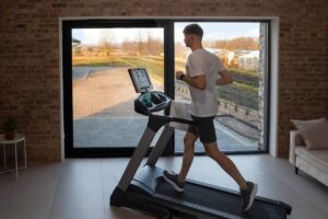 Young man running on a treadmill in a modern home with large windows and a rural view.