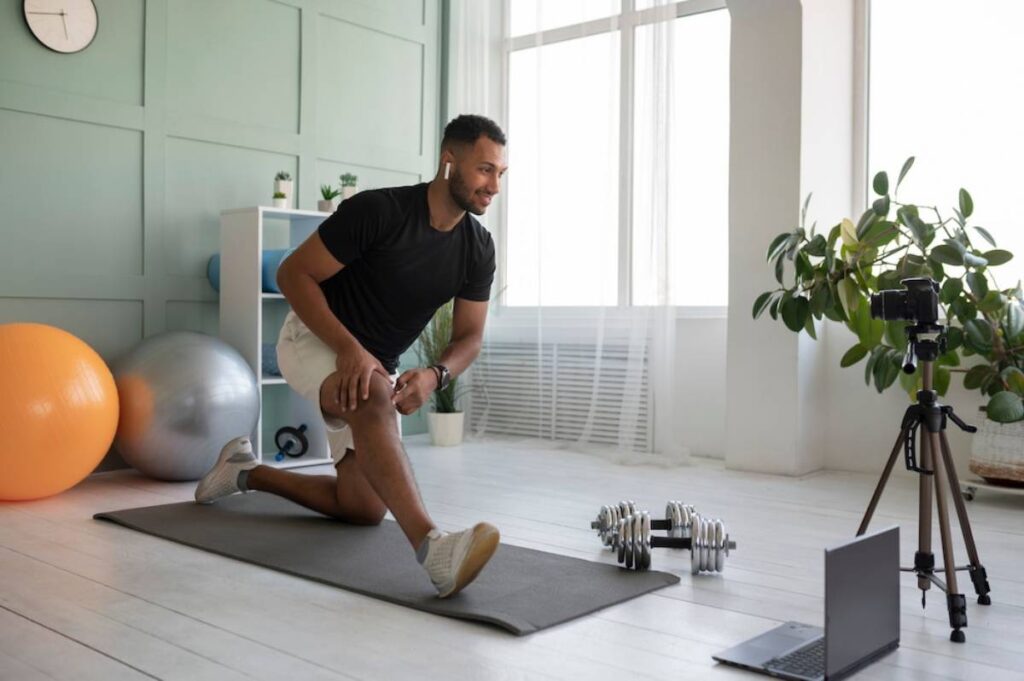 Man stretching in a home gym while recording a video with a smartphone mounted on a tripod.