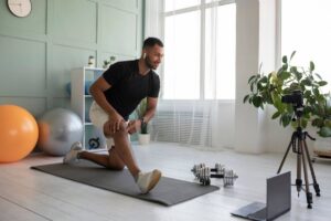 Man stretching in a home gym while recording a video with a smartphone mounted on a tripod.
