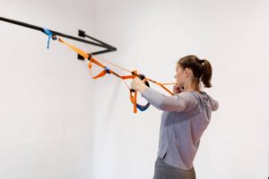 Young woman exercising using a suspension trainer in a bright indoor gym.