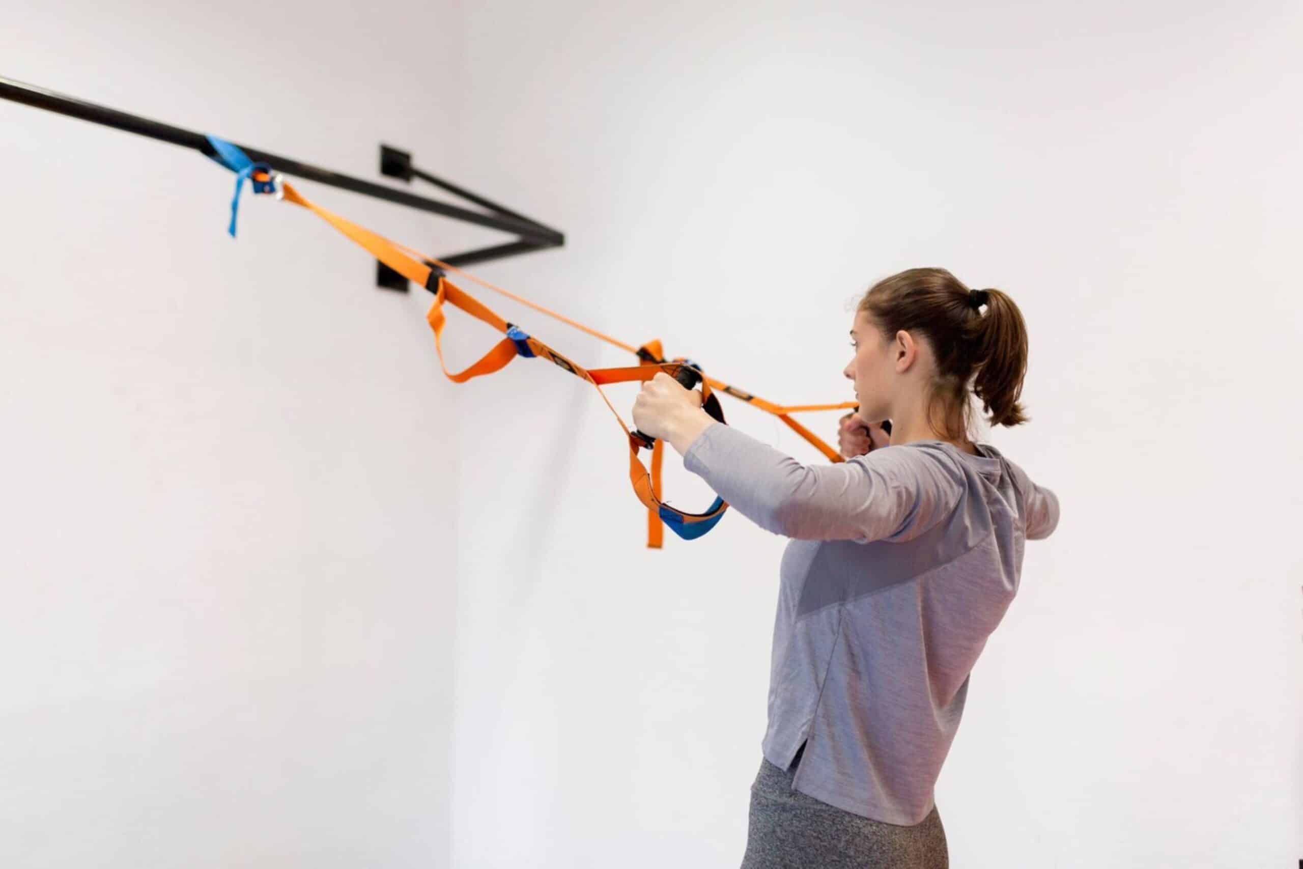 Young woman exercising using a suspension trainer in a bright indoor gym.