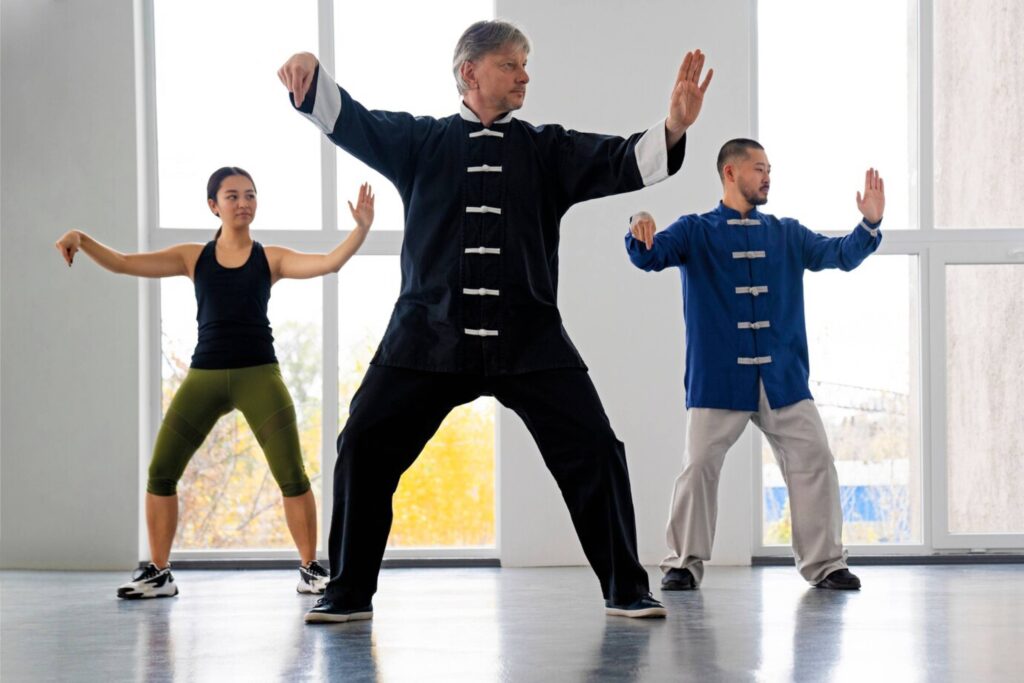 Three people practicing Tai Chi in a bright studio, with large windows in the background.