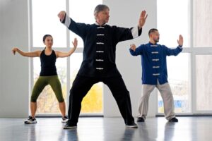 Three people practicing Tai Chi in a bright studio, with large windows in the background.