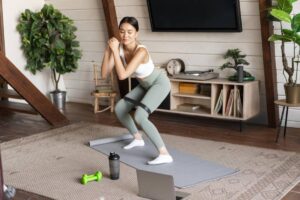 A woman exercising at home with resistance bands, surrounded by indoor plants and exercise equipment.
