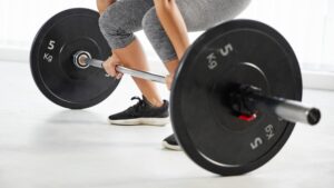 Person lifting a barbell with 5 kg weights in a bright gym.