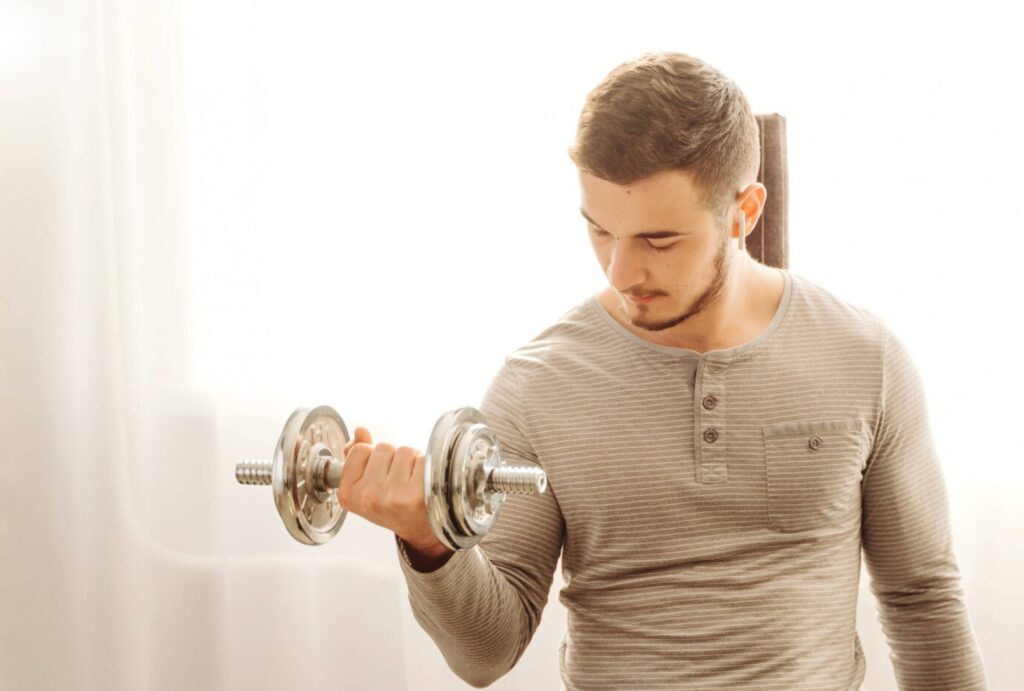 Young man lifting a dumbbell indoors, focused on his exercise, in a well-lit room.