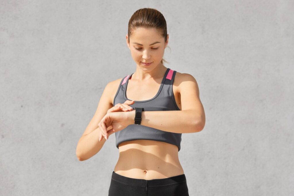 Young woman in sports attire checking fitness tracker against a plain background.