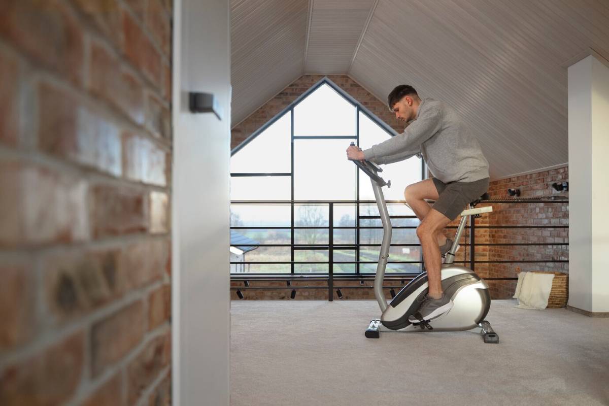 Man exercising on a stationary bike in a loft with brick walls and large windows. 