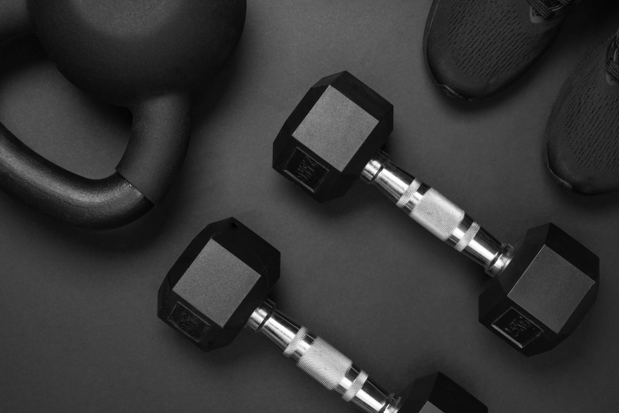  Black dumbbells, kettlebell, and training shoes arranged on a dark surface.