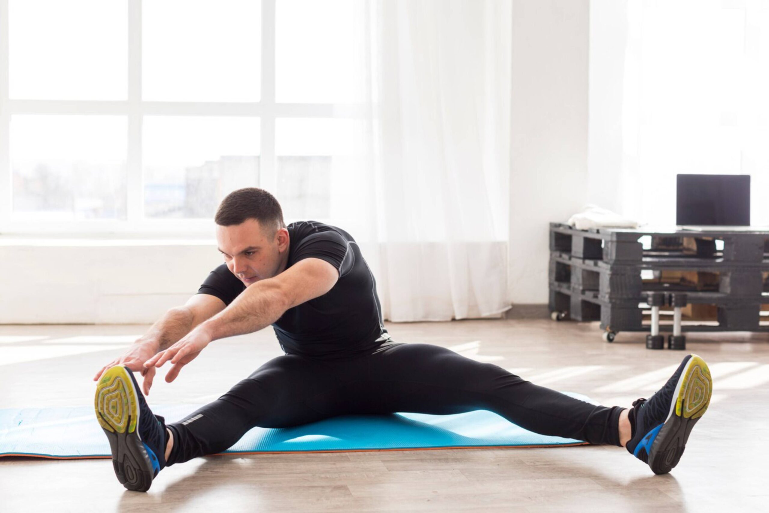  Man stretching in a bright room, reaching towards his foot on a blue mat.