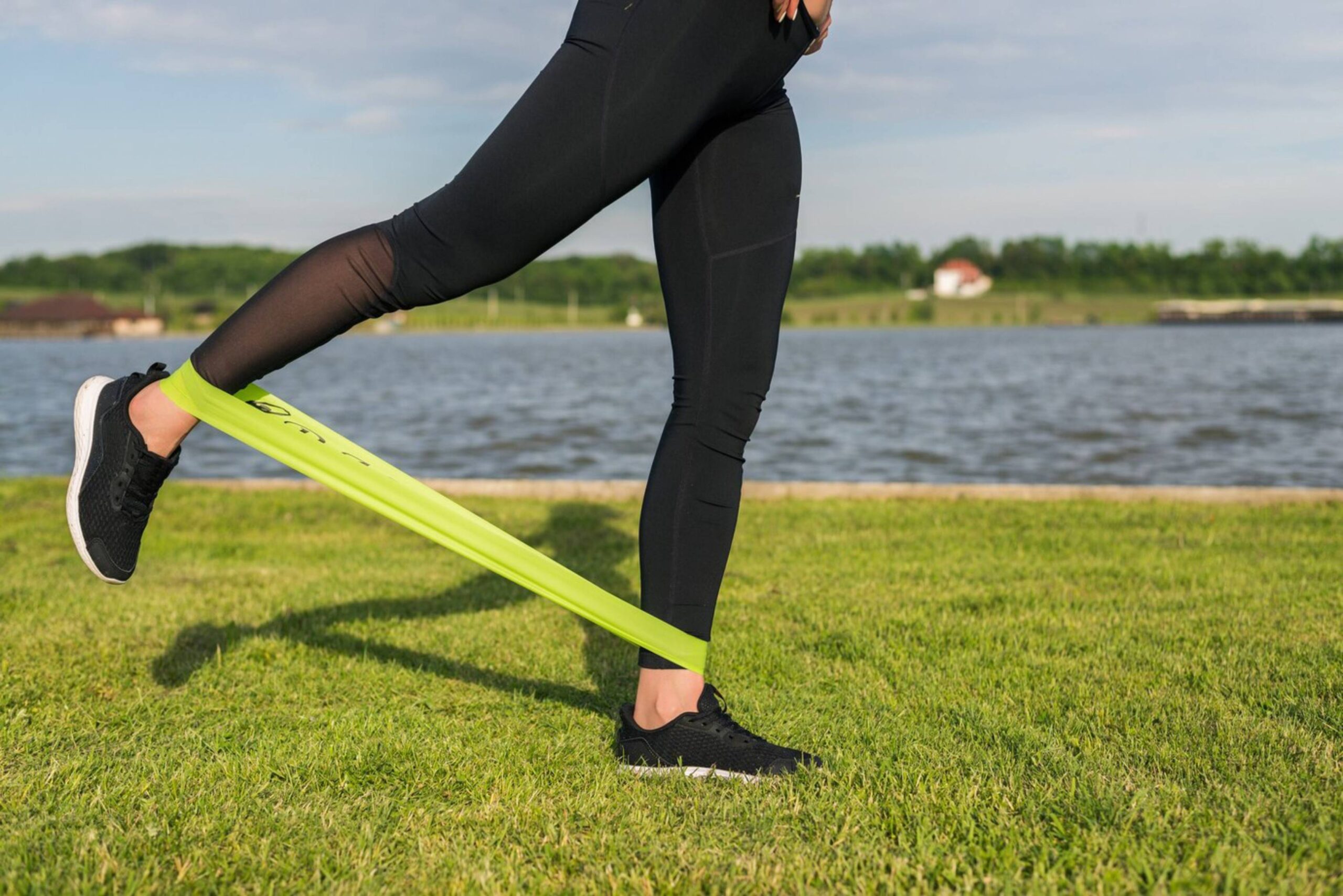 A person exercises by a lake using a resistance band around their leg. 