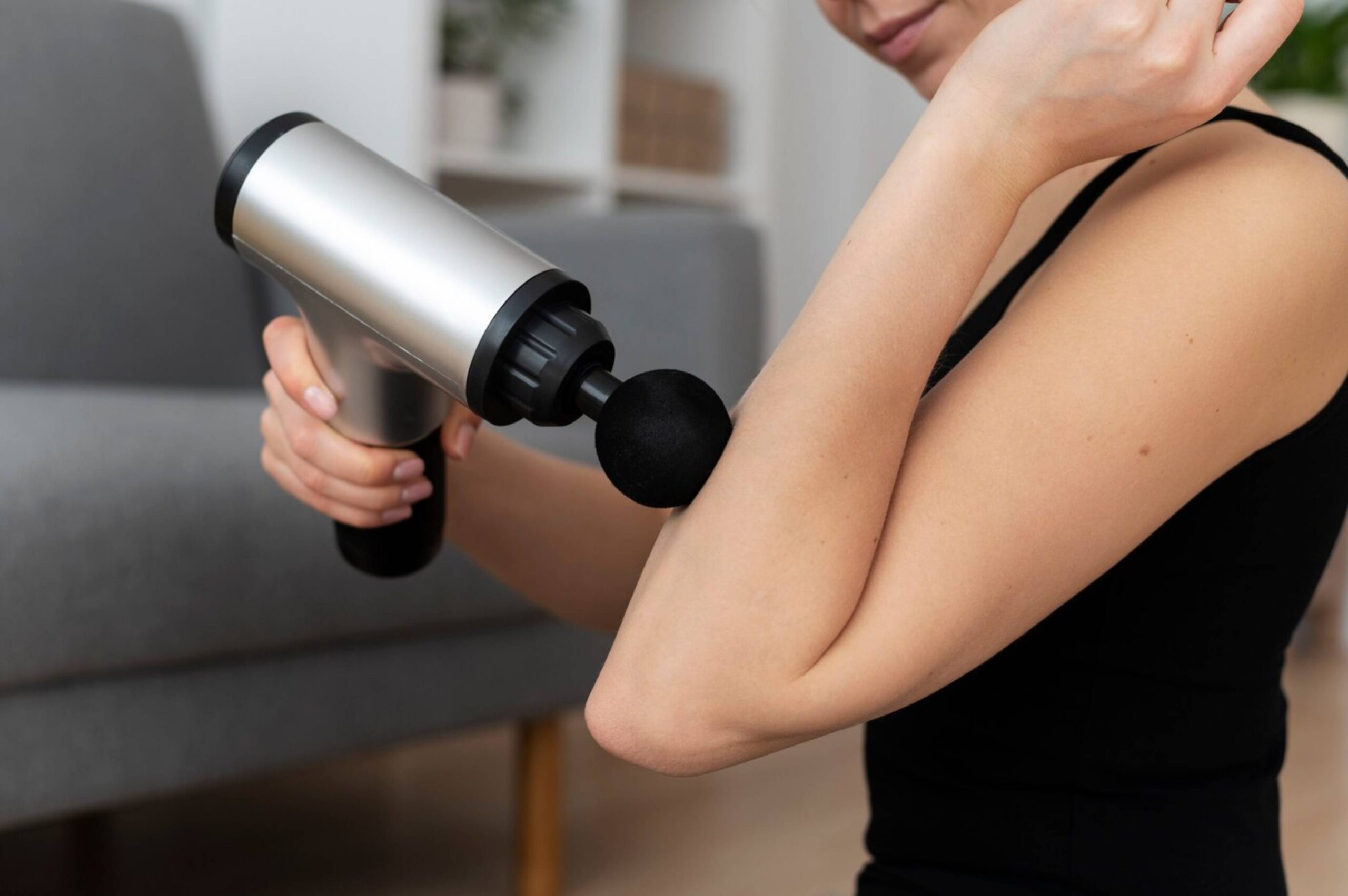  A person using a handheld massage gun on their shoulder to relieve muscle tension.