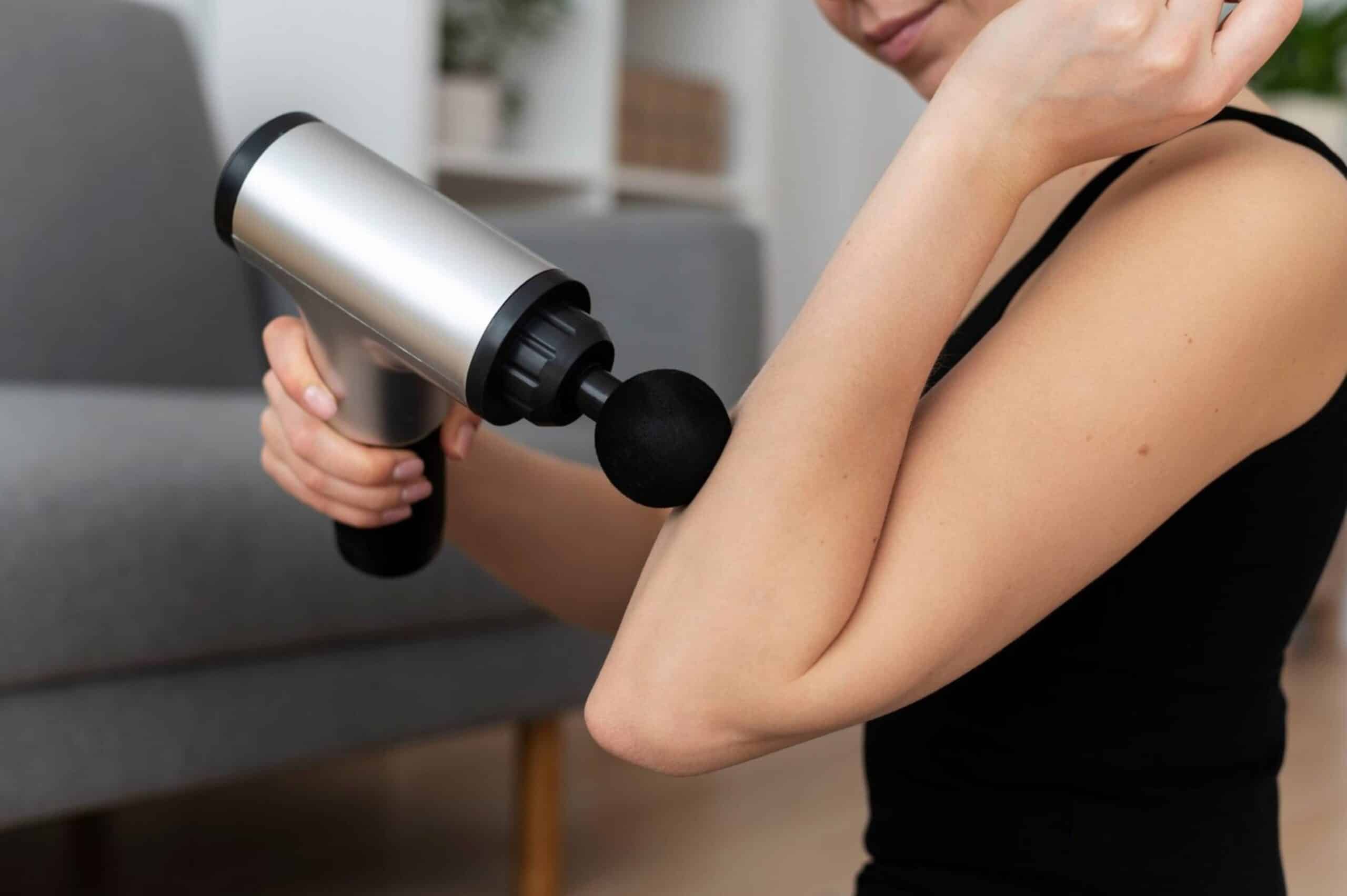 A person using a handheld massage gun on their shoulder to relieve muscle tension.