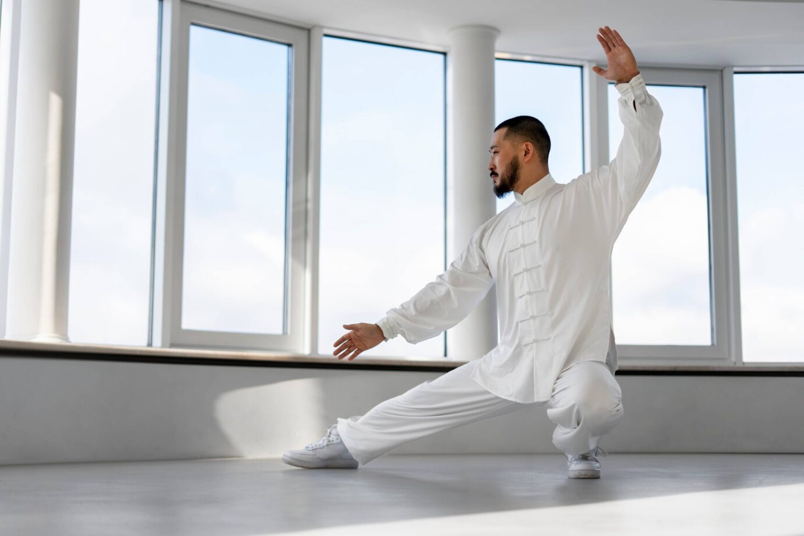 Man performing Tai Chi in a bright room with large windows. 