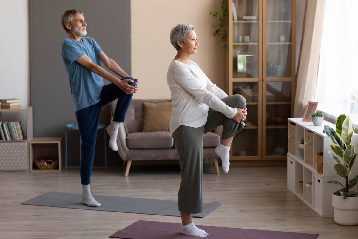 Elderly couple performing stretching exercises on yoga mats in a cozy living room.