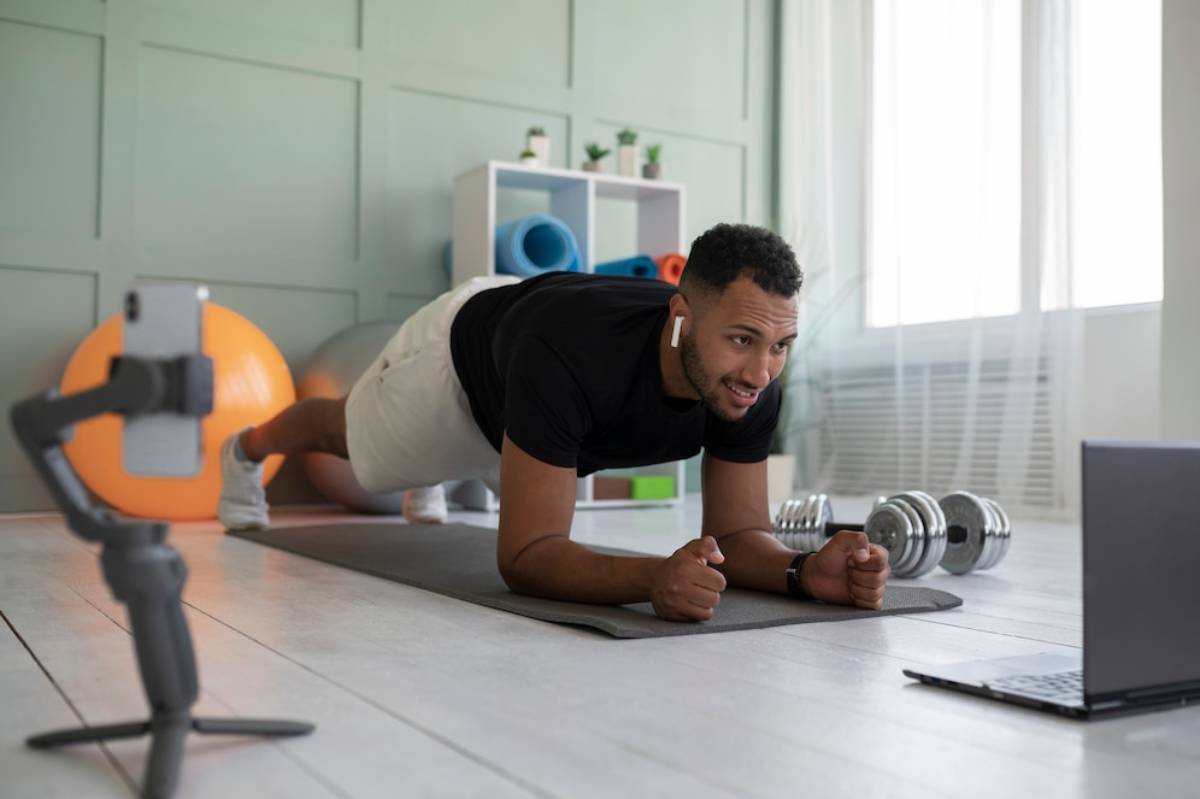  Man doing a plank exercise at home while watching an online workout video on a laptop.