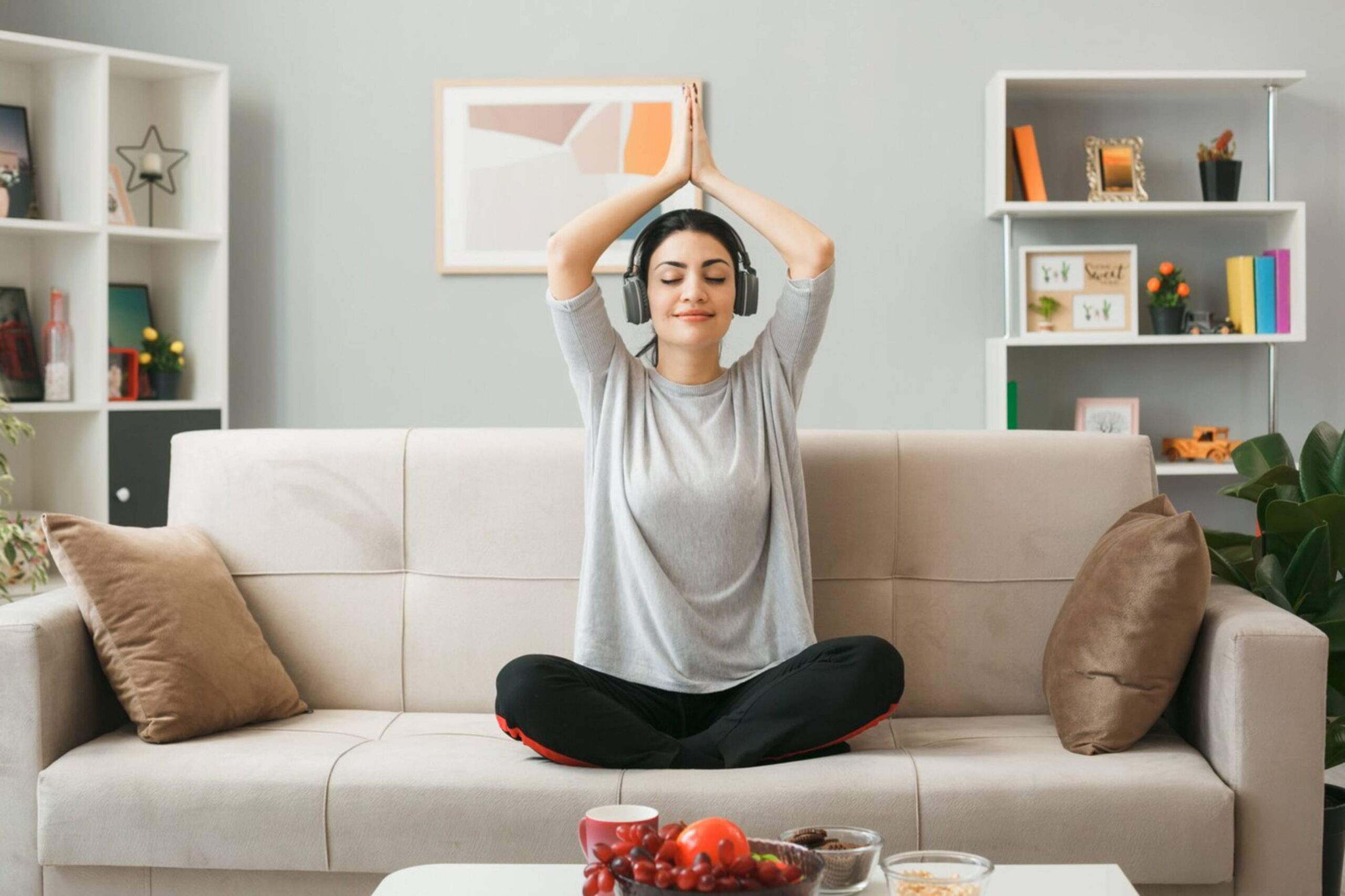  Woman meditating on a sofa with headphones in a modern living room.