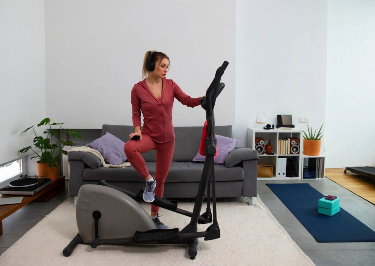 Woman in red sportswear using an elliptical machine in a home living room.