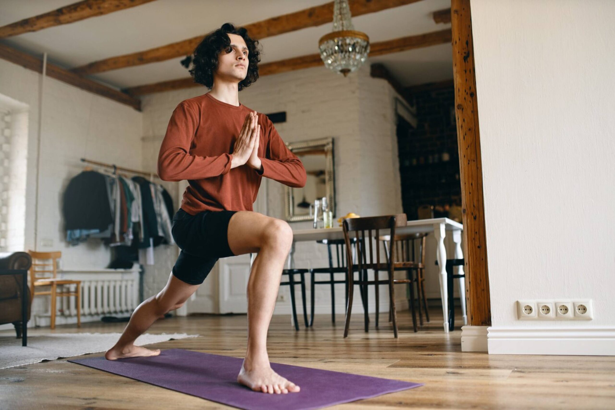  Man practicing yoga in a spacious room, performing a warrior pose on a purple mat.