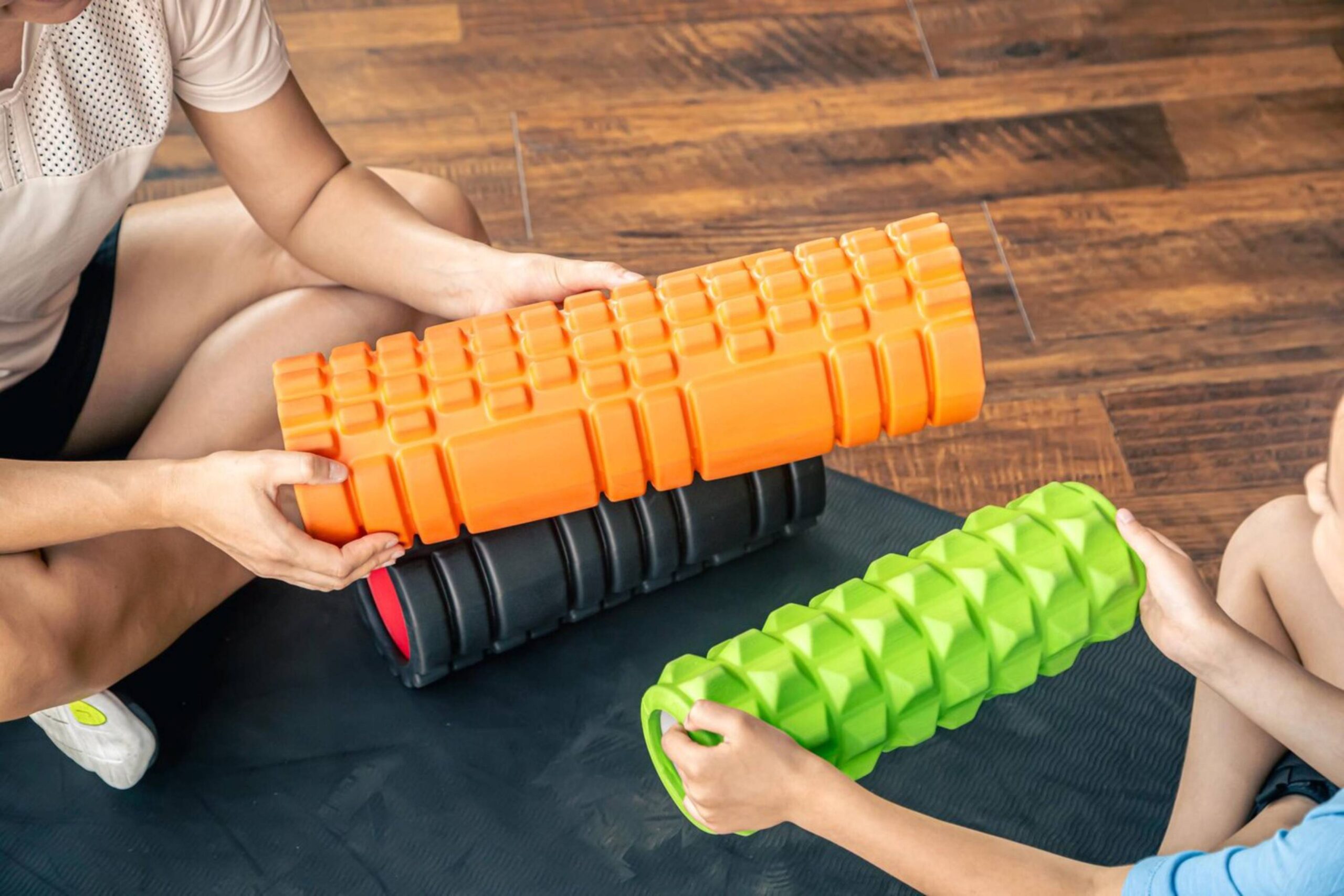 Two people using textured foam rollers for muscle massage in a gym setting. 