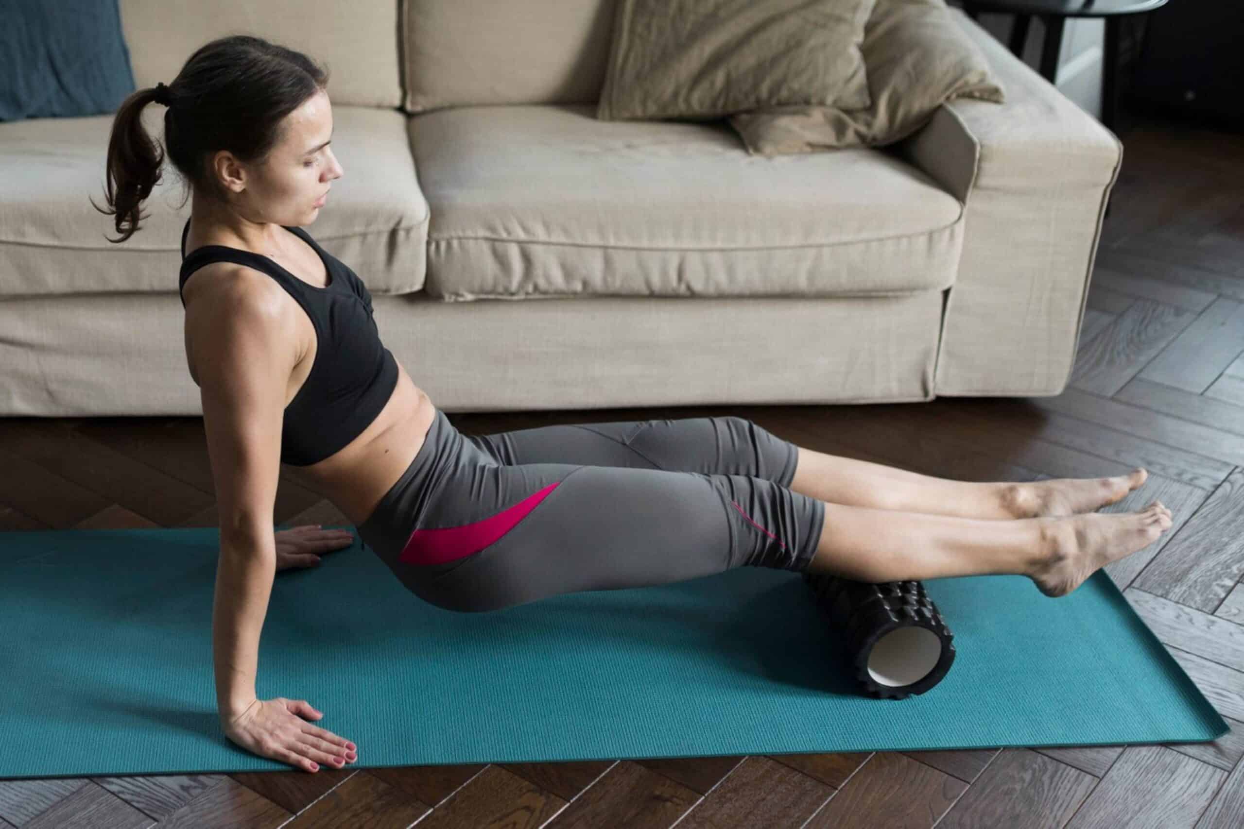 Woman performing a muscle stretch using a foam roller on a yoga mat at home.