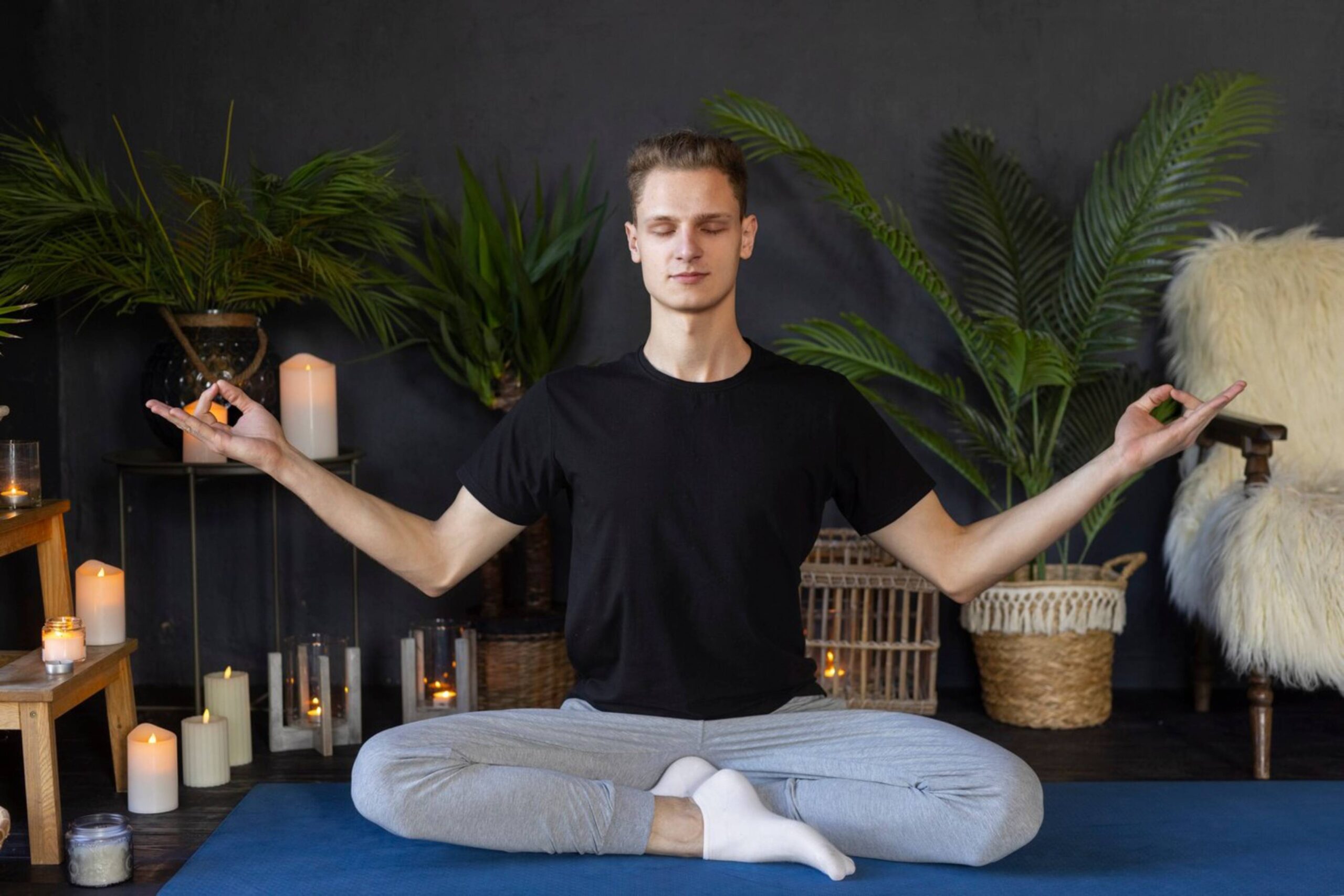  Young man meditating in a serene room with candles and potted plants.