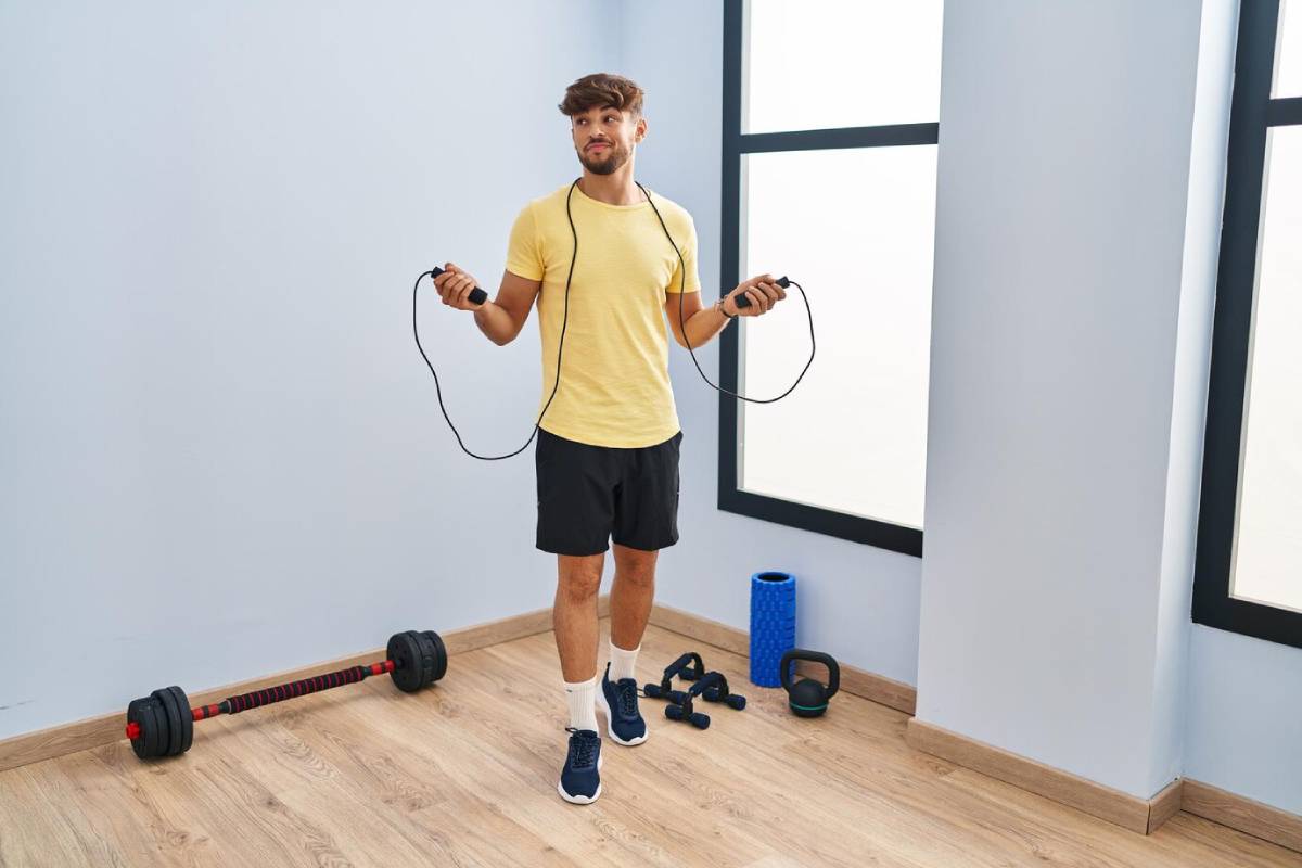  Young man holding a jump rope in a gym, surrounded by fitness equipment.
