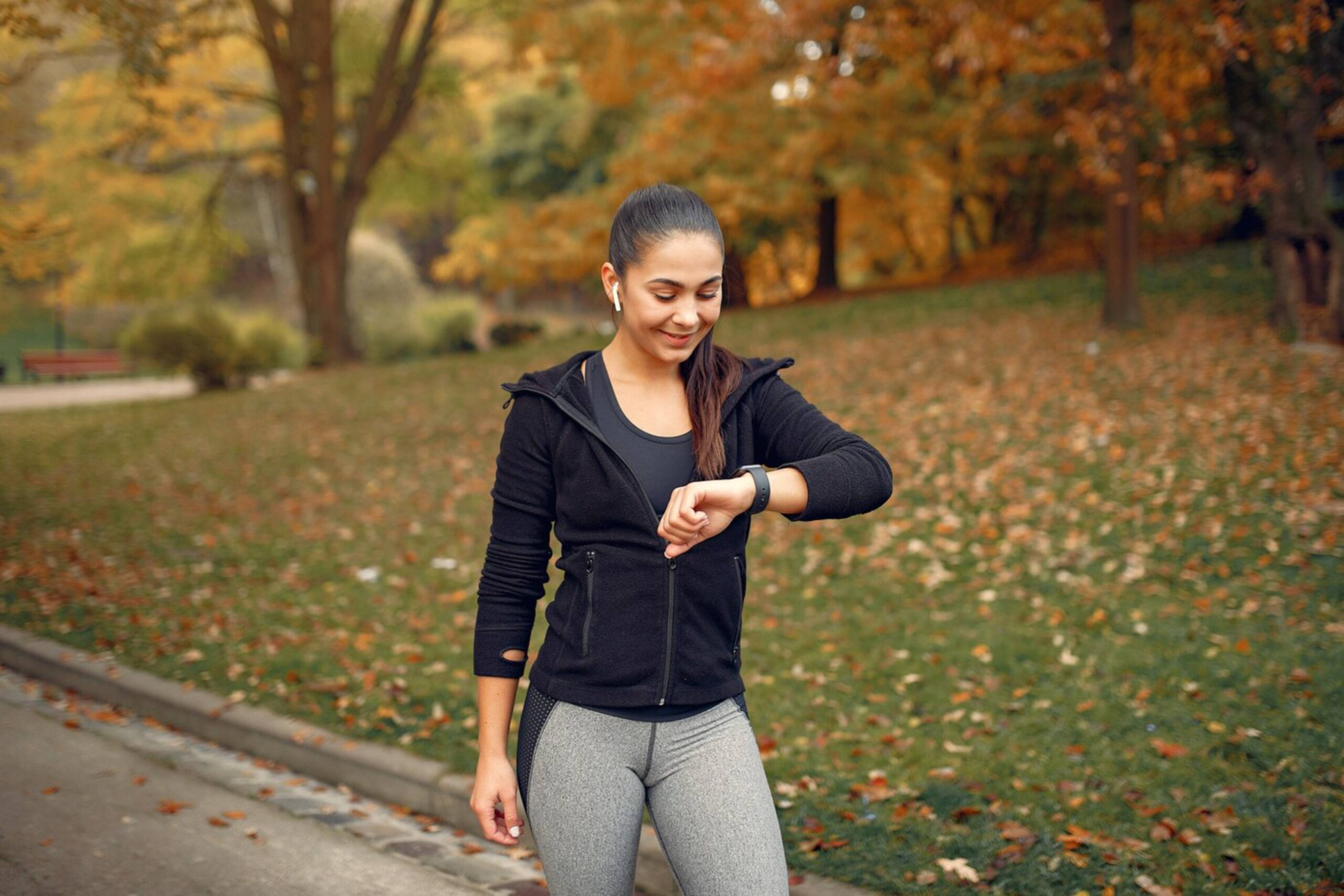  Woman in sportswear checking fitness watch in autumnal park.