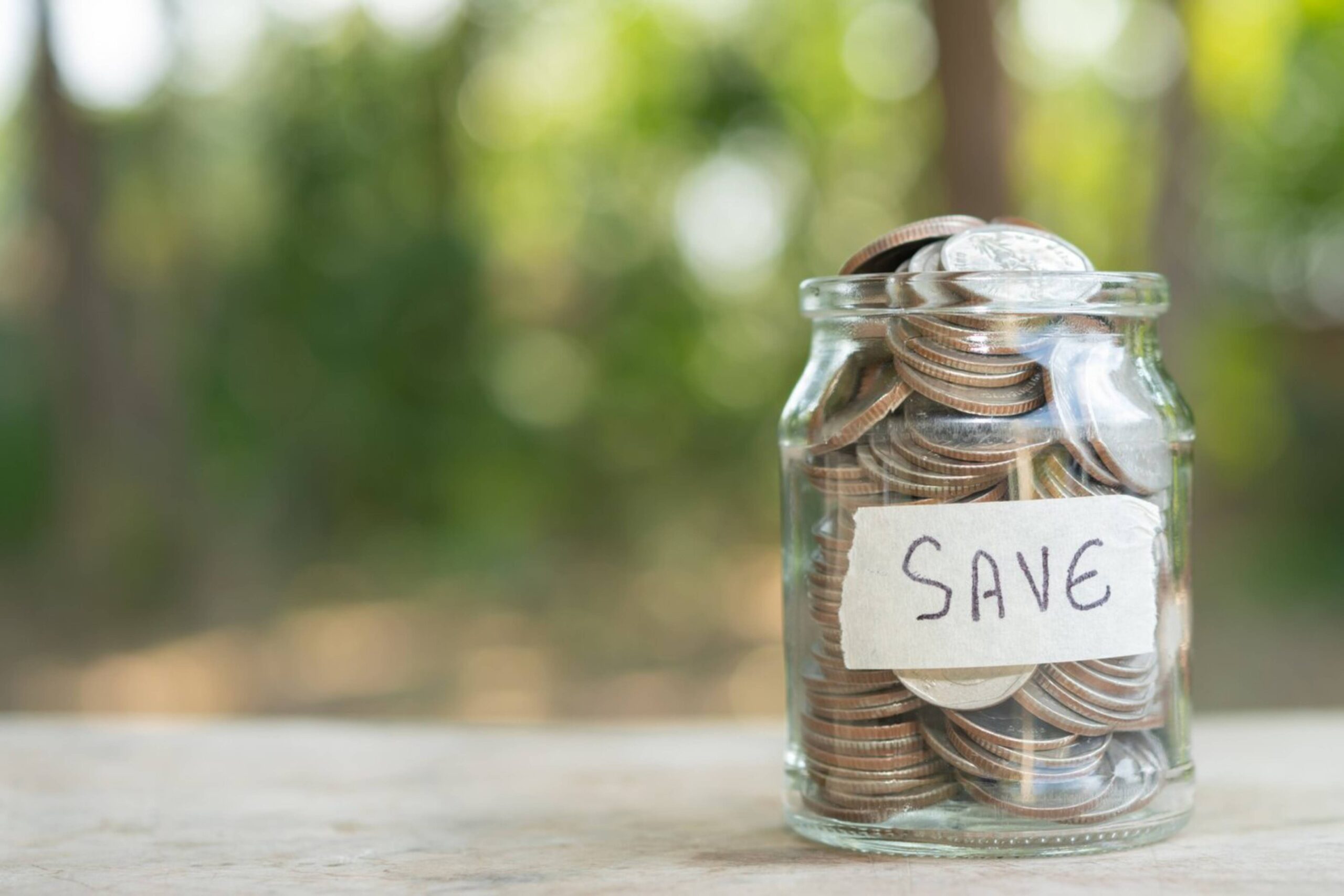Glass jar filled with coins and labeled save set against a blurred green background. 