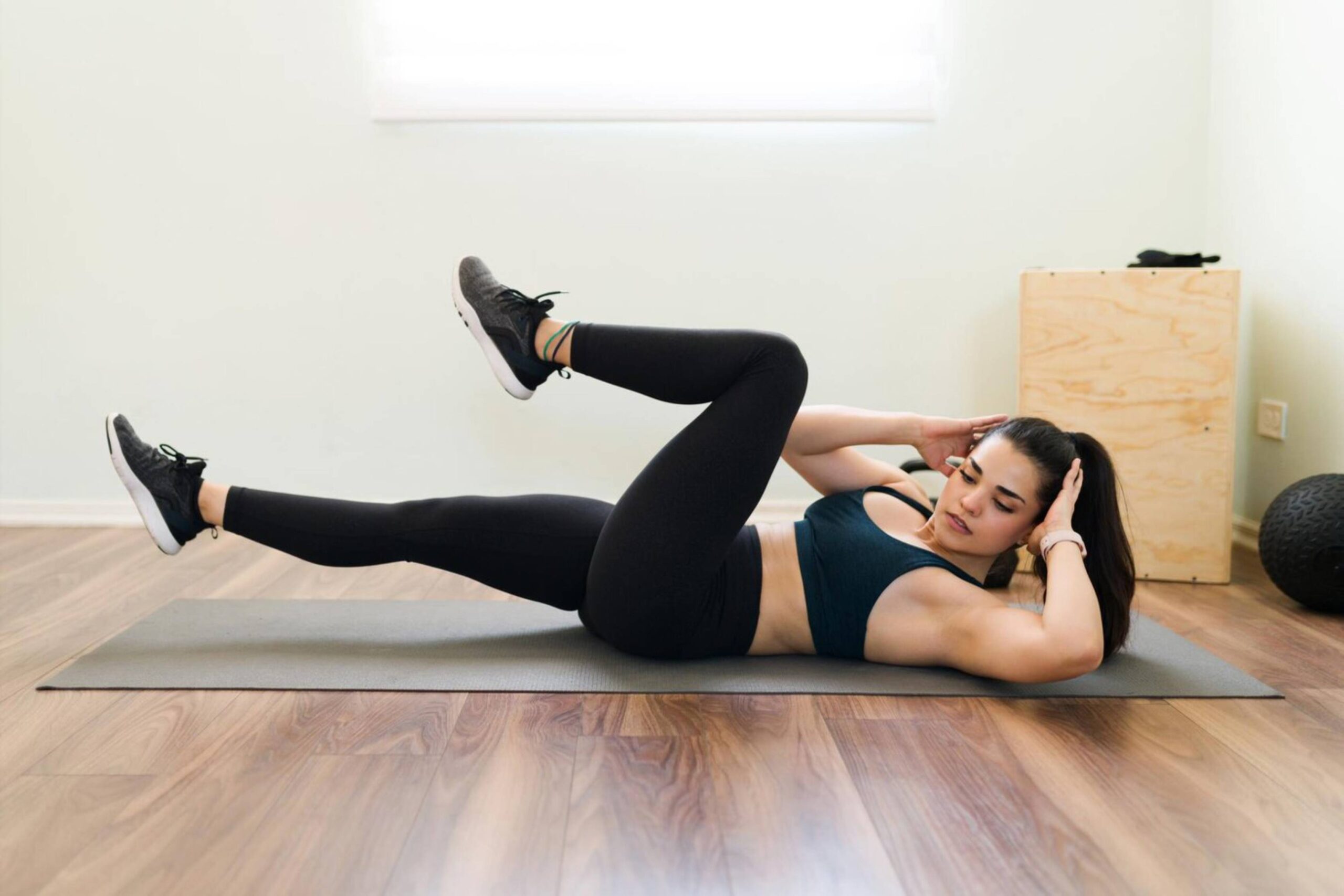  Woman performing abdominal exercises on a mat in a bright gym room.