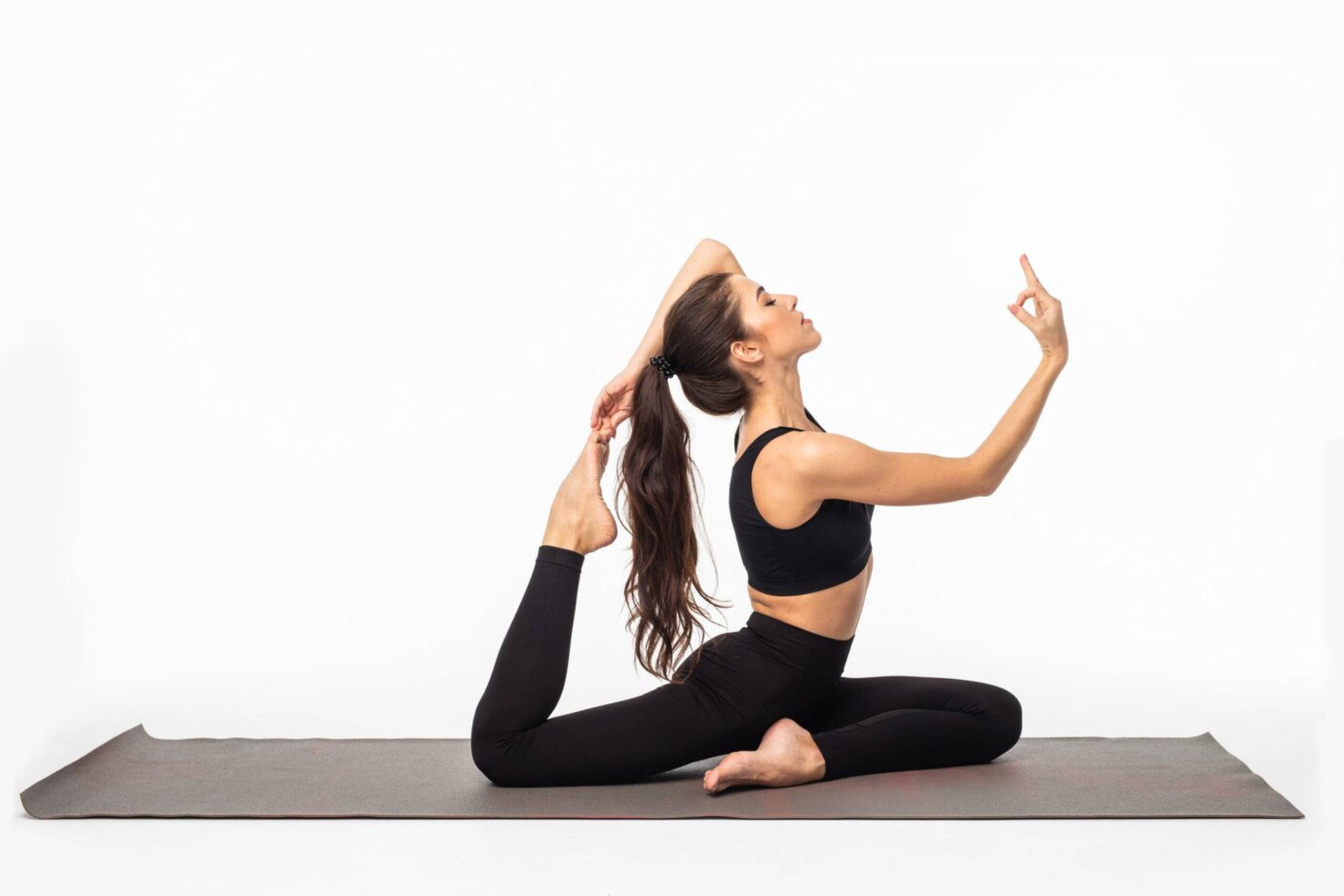 Woman performing an advanced yoga pose on a mat against a white background. 