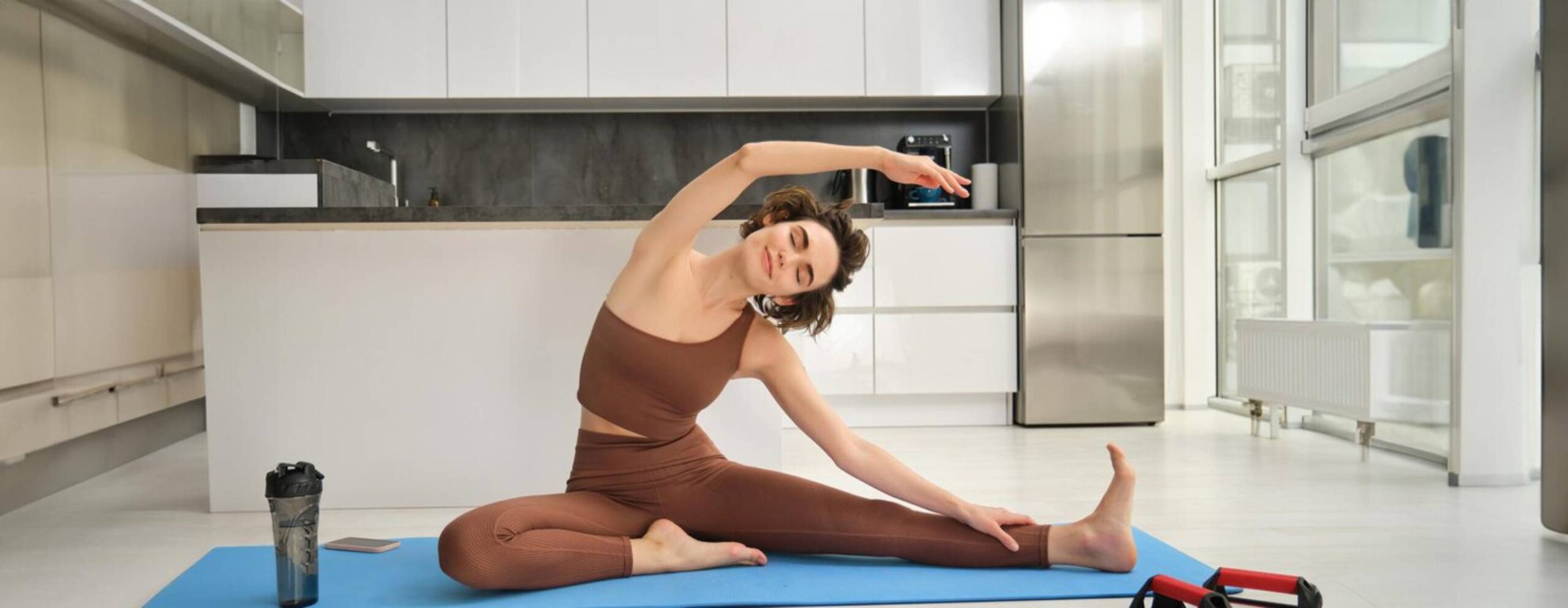 Young woman stretching on a yoga mat in a modern kitchen. 