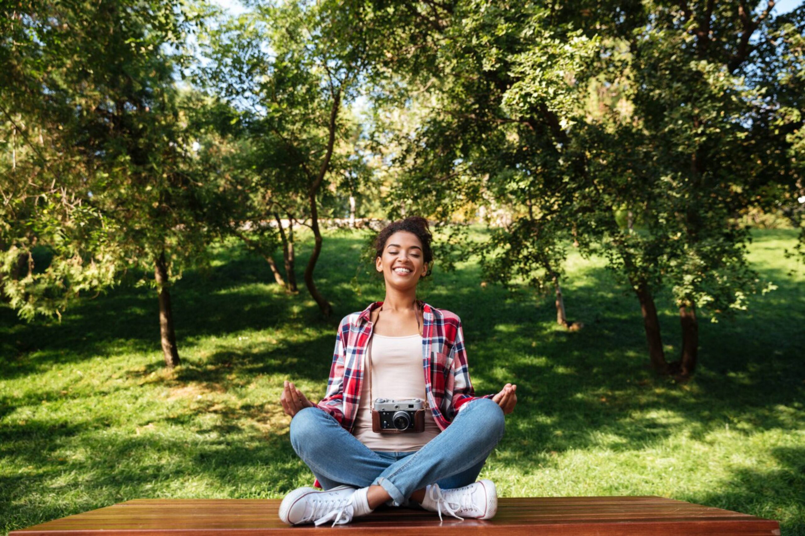 Young woman meditating peacefully on a bench in a lush green park. 