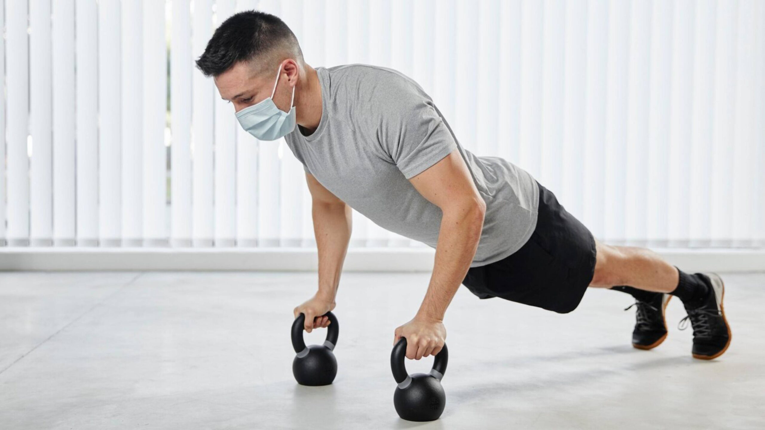 Man in mask doing push-ups with kettlebells in a gym. 