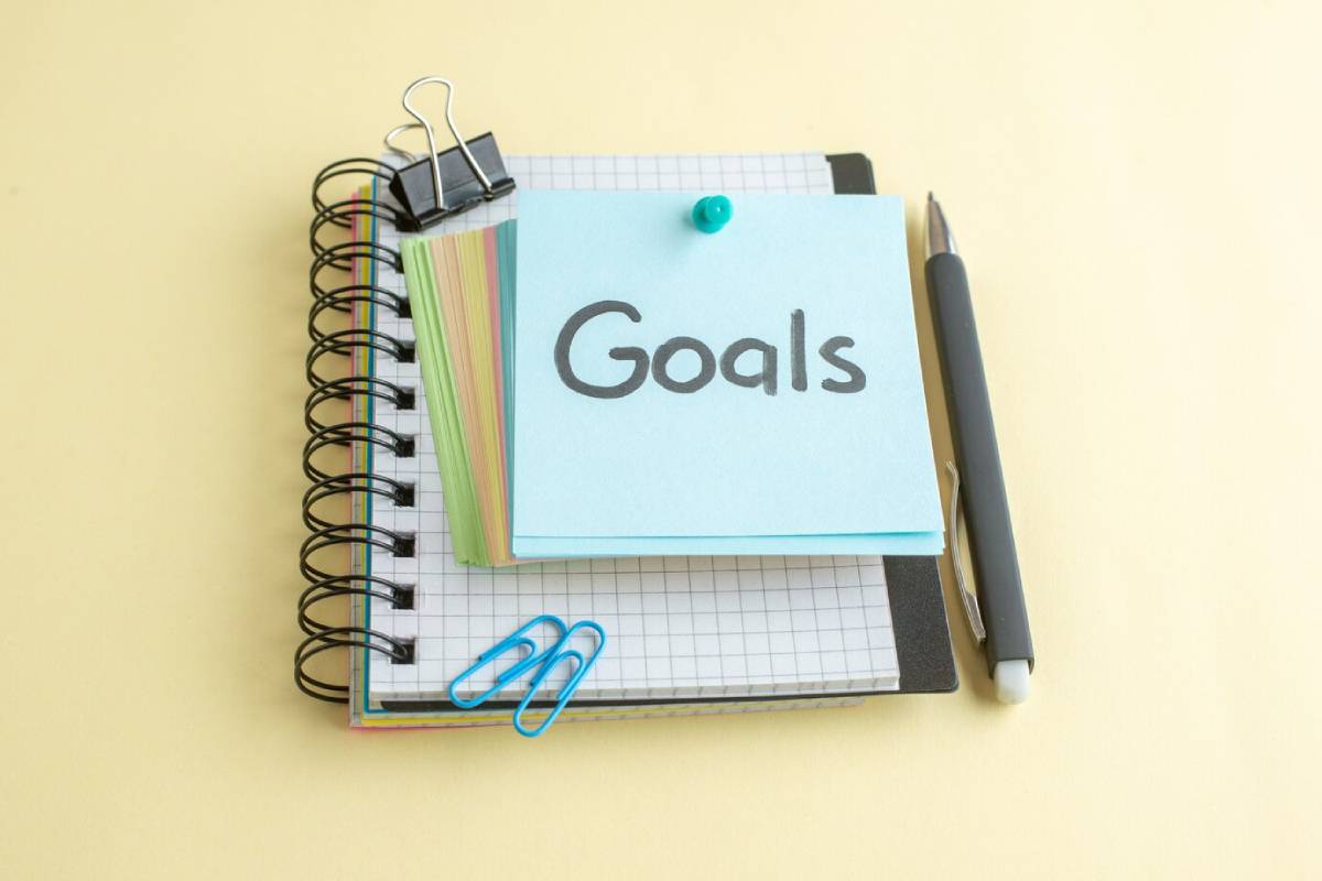 Goals written in a notebook with a pen and paper, set against a bright yellow background. 
