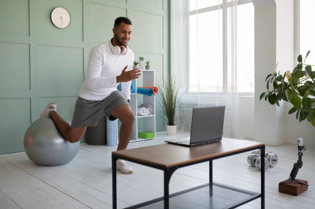 Man exercising in a home office, using an exercise ball and interacting with a laptop on a desk. 