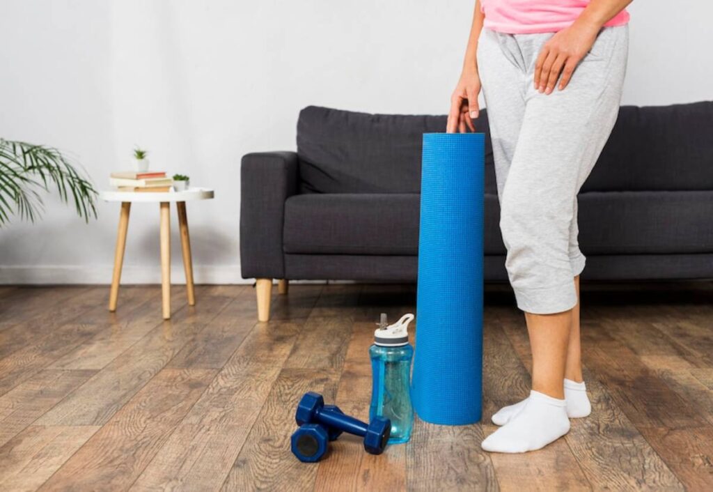A woman stands beside a yoga mat and a water bottle.