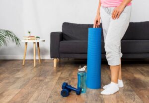 A woman stands beside a yoga mat and a water bottle.