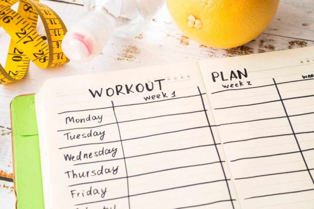 Workout plan on a notebook beside a lemon and a measuring tape, symbolizing health and fitness goals.