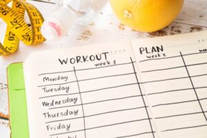 Workout plan on a notebook beside a lemon and a measuring tape, symbolizing health and fitness goals.